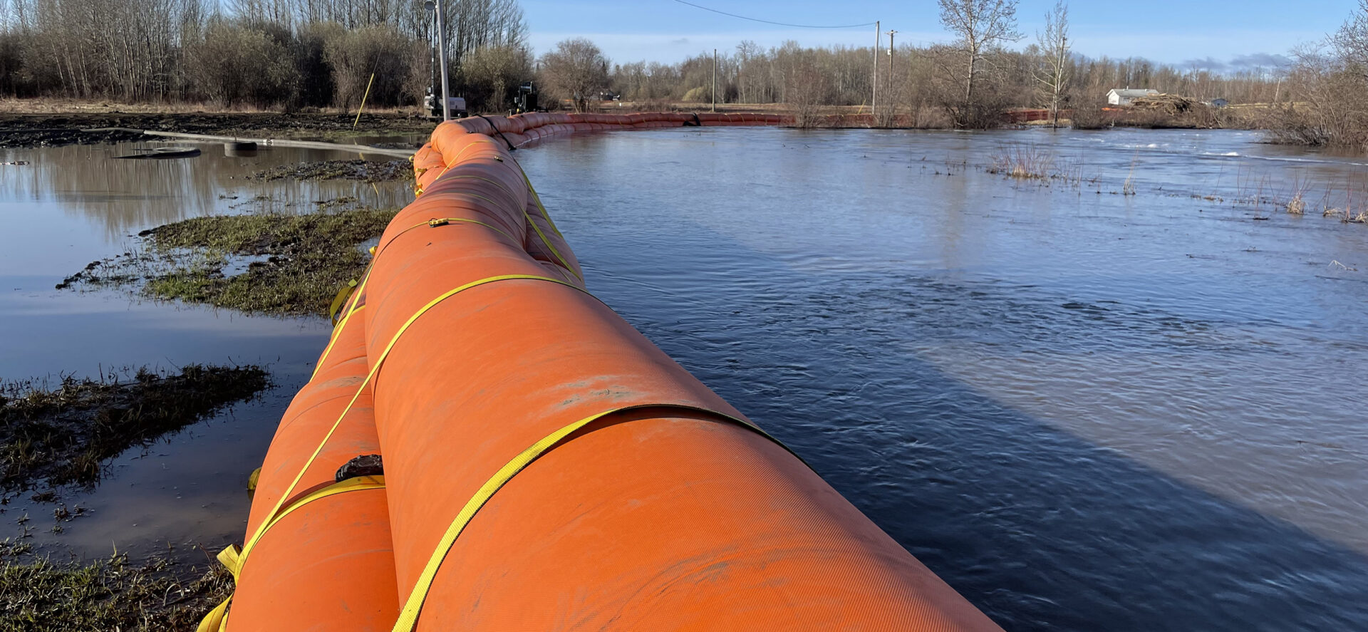 Orange inflatable flood barrier across flooded roadway