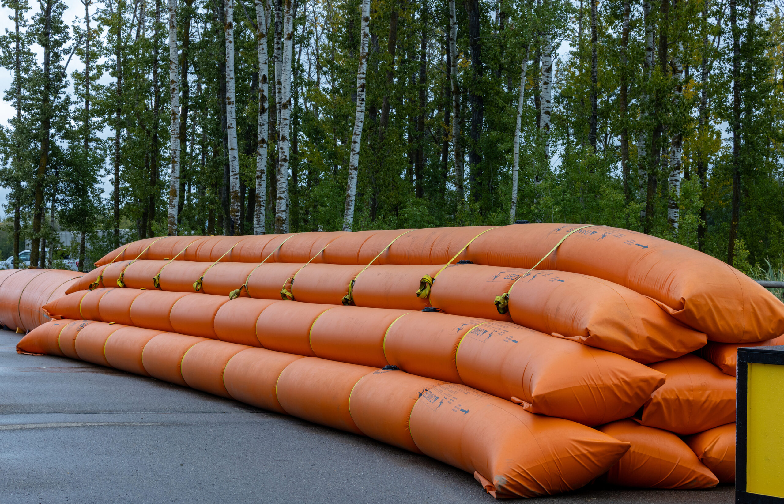 Stacked orange inflatable flood barriers outdoors near trees