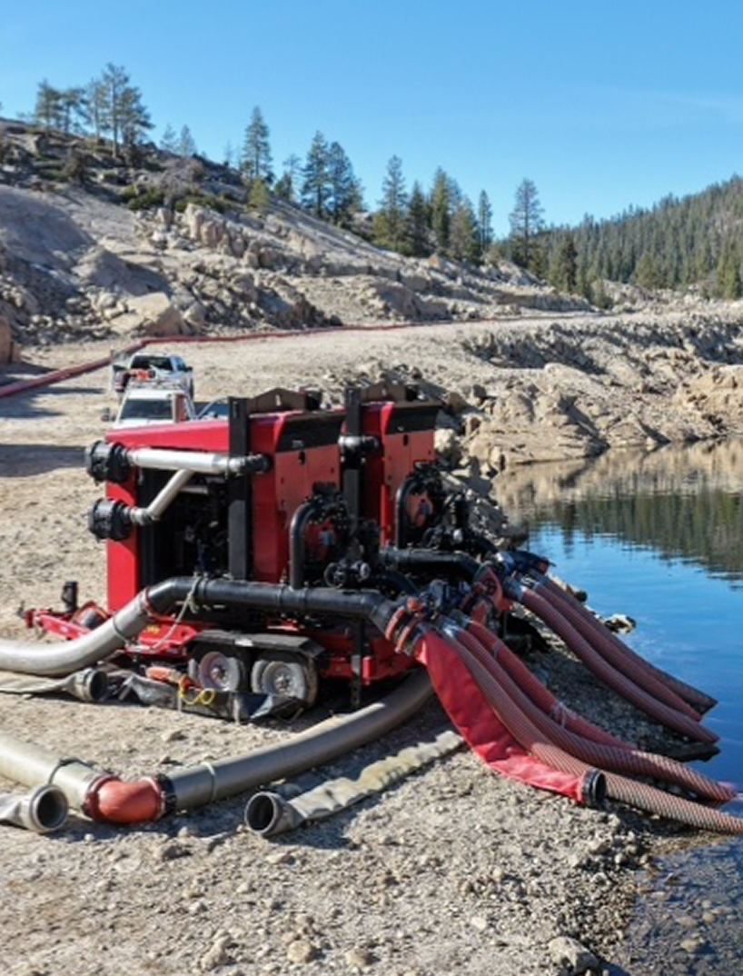 Red industrial water pump with hoses by lakeside